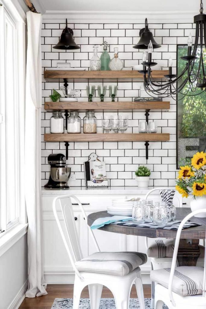 subway tile backsplash with wood floating shelves and a wood table under black chandelier 