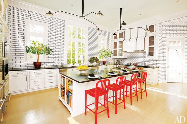 This kitchen has light wood floors, white cabinets, and white subway tile with black countertops, all accented with bright red chairs.