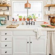 A white farmhouse kitchen that showcases vintage tile floors, a copper lighting fixture, and open shelves.