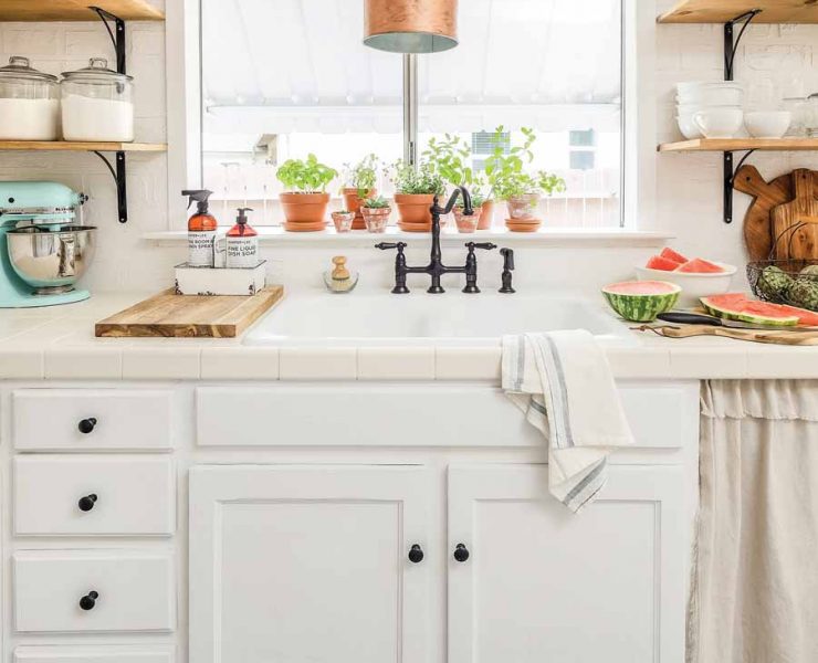 A white farmhouse kitchen that showcases vintage tile floors, a copper lighting fixture, and open shelves.
