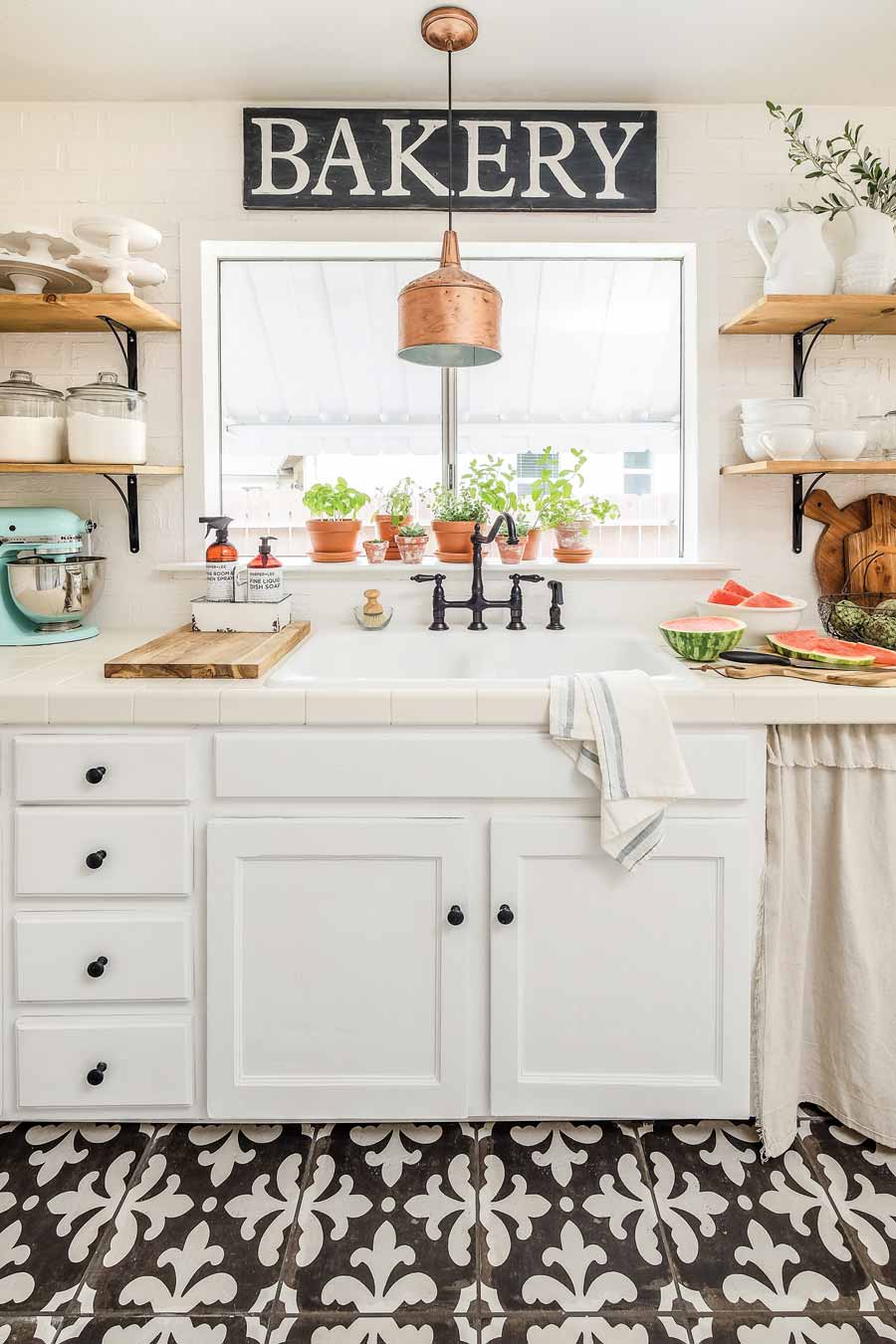 A white farmhouse kitchen that showcases vintage tile floors, a copper lighting fixture, and open shelves.