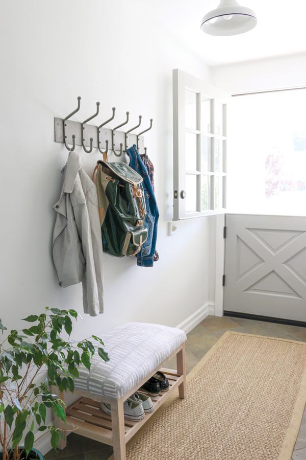 A home entryway with 6 hanger racks holding a white jacket green backpack and blue jeans jacket 