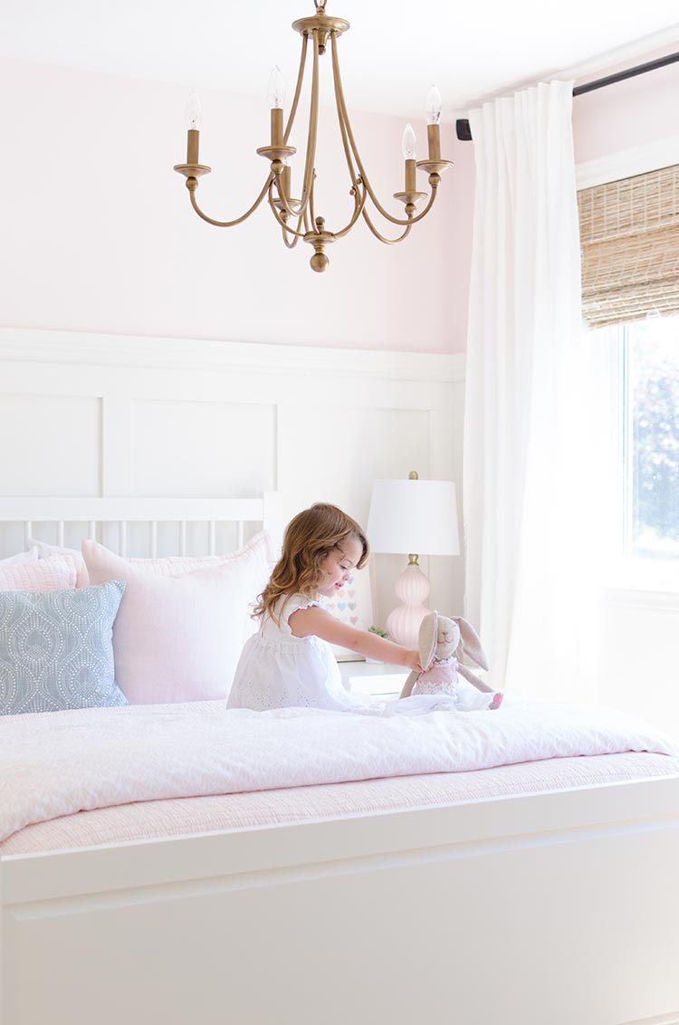 clutter free décor in a girl’s bedroom with pink walls, white wainscoting and wood chandelier