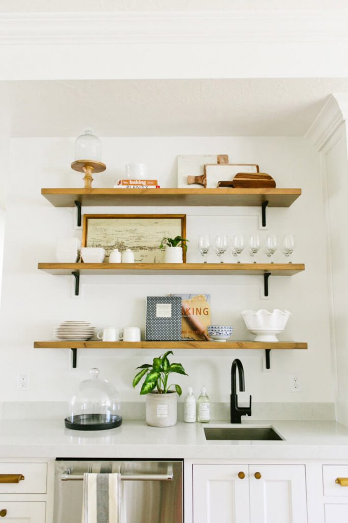 Three open shelves that showcase various glasses and dishes in a farmhouse kitchen.