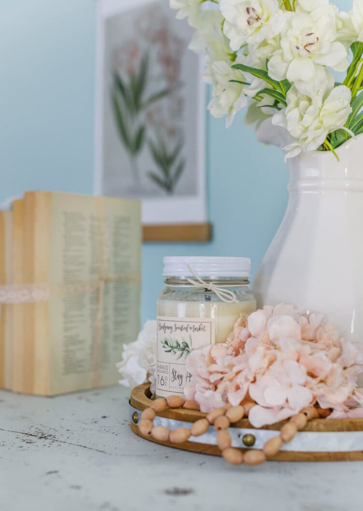 Shabby dresser top with rustic wood tray, jug of spring flowers and candle.