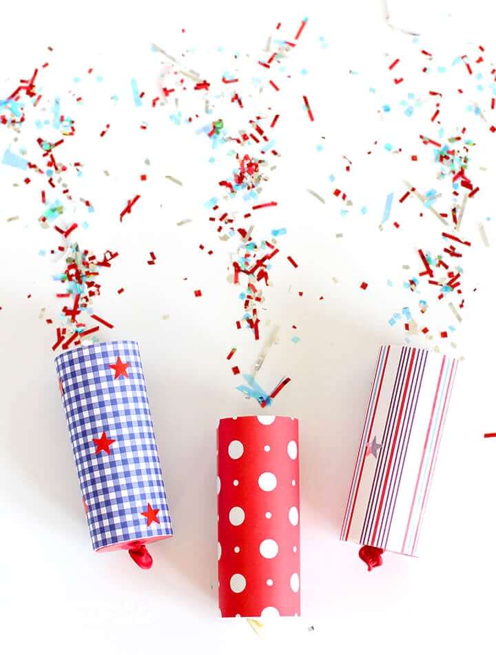 A row of three red, white, and blue Fourth of July confetti poppers, surrounded by a mix of different colored confetti