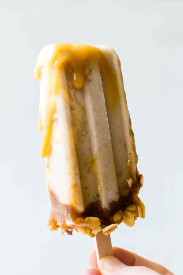 Hand holding a banoffee ice cream popsicle drizzled with a creamy caramel sauce