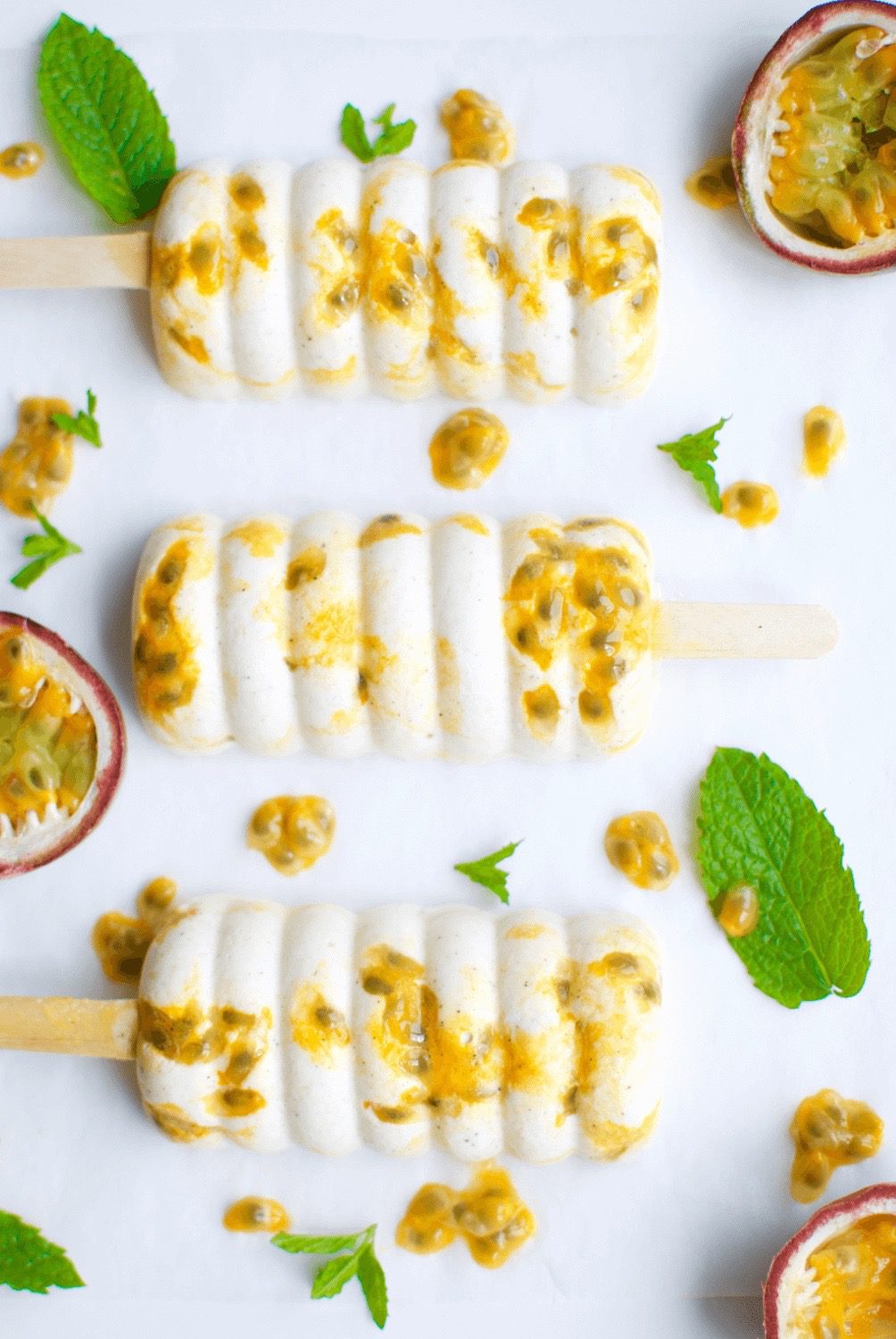 A tropical popsicle row surrounded by loose passionfruits, seeds, and mint