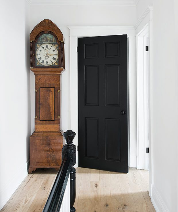 A tall, auburn-colored Grandfather clock resting next to a decorative black door