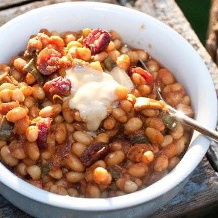 A steaming bowl of Fourth of July maple baked beans with a spoon protruding upward