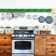 A stove, an American-made appliance, surrounded by several wooden fixtures and a collection of pots hanging above