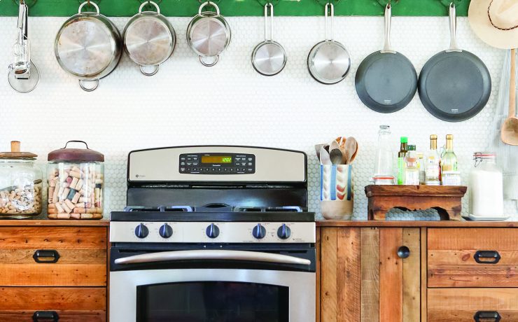 A stove, an American-made appliance, surrounded by several wooden fixtures and a collection of pots hanging above