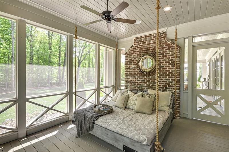 A large bed dangles from ropes feet away from the home's wraparound porch