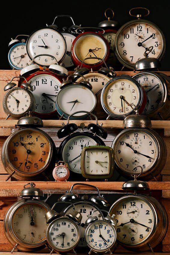 A collection of vintage clocks placed upon four separate shelves