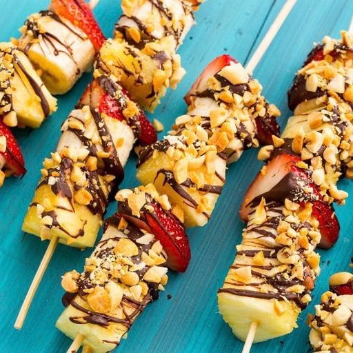 A row of Fourth of July Kebabs complete with bananas, strawberries, pineapples, a chocolate drizzle, and peanuts