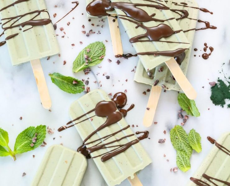 A mint chocolate popsicle collection surrounded by mint leaves and cacao nibs