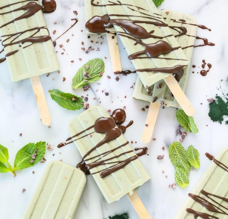 A mint chocolate popsicle collection surrounded by mint leaves and cacao nibs