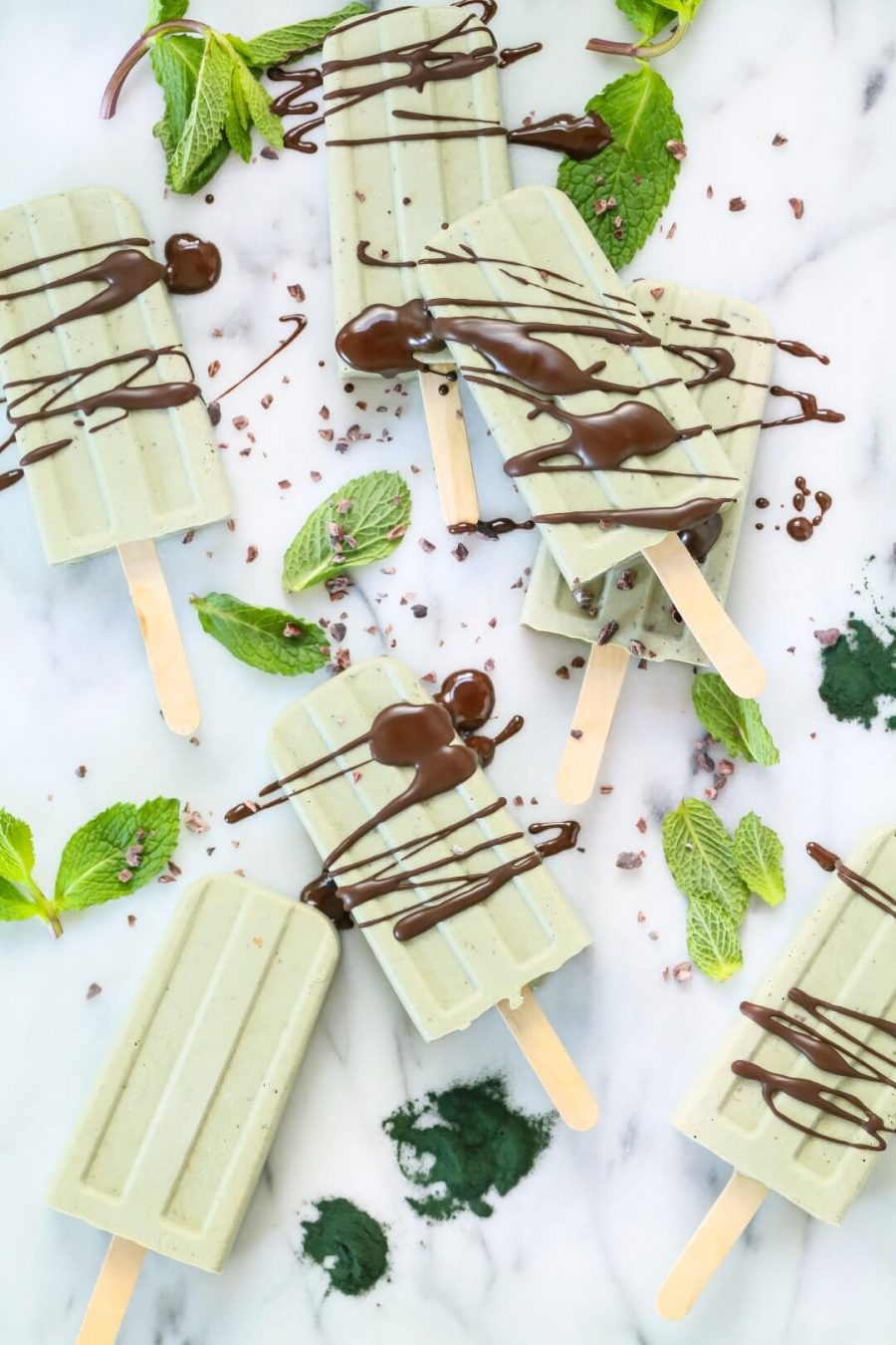 A mint chocolate popsicle collection surrounded by mint leaves and cacao nibs