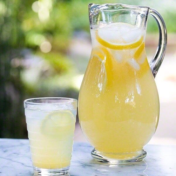 A glass of Fourth of July lemonade seated next to a larger pitcher of lemonade