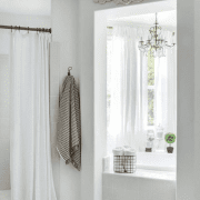 A white master bathroom with a large window and shower and stenciled tiles