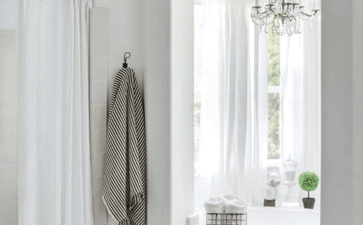 A white master bathroom with a large window and shower and stenciled tiles