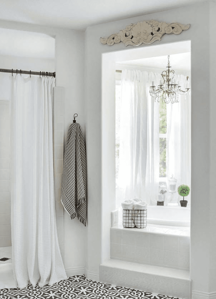 A white master bathroom with a large window and shower and stenciled tiles