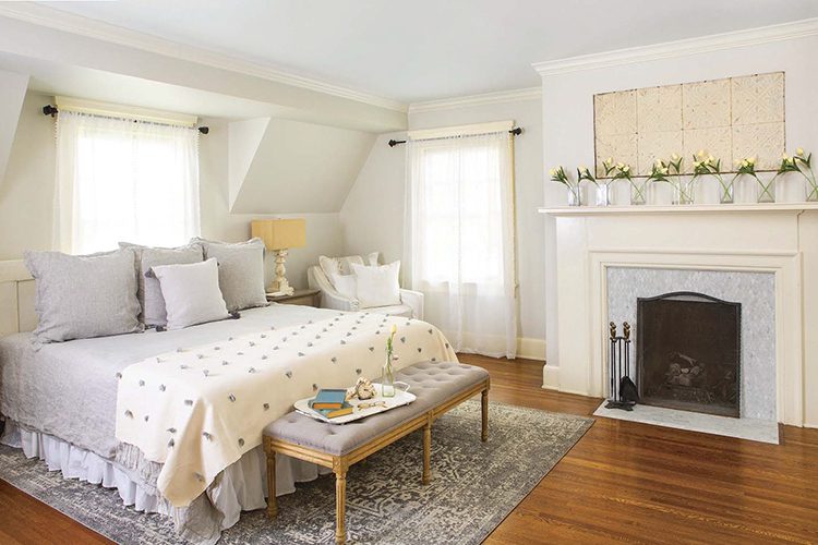 A renovated farmhouse master bedroom with a fireplace and hardwood floors