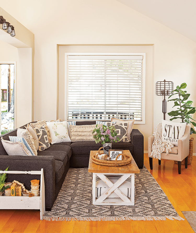 Small living room with gray couch, throw pillows, patterned rug, and farmhouse details.