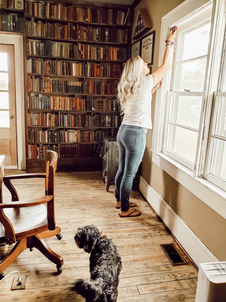 A woman and her dog stand in front of a sunny window