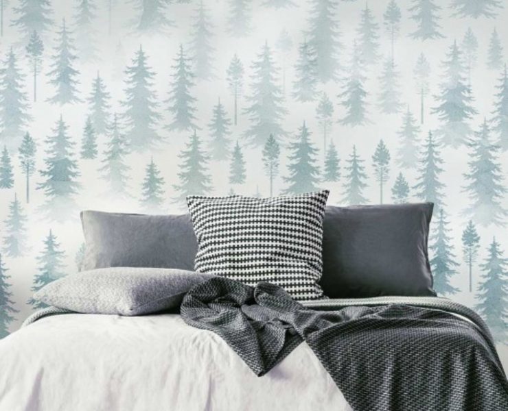 A wall mural made of many layers of tree stencils behind a bed.