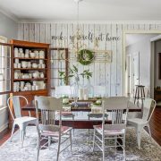 Dining room with white shiplap accent wall. Wooden cabinet displays many cream-colored dishes.