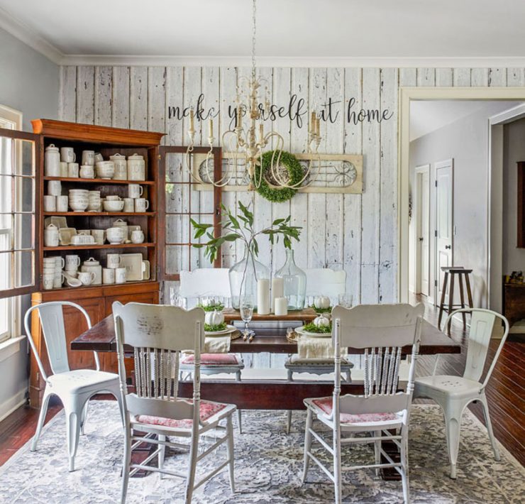 Dining room with white shiplap accent wall. Wooden cabinet displays many cream-colored dishes.