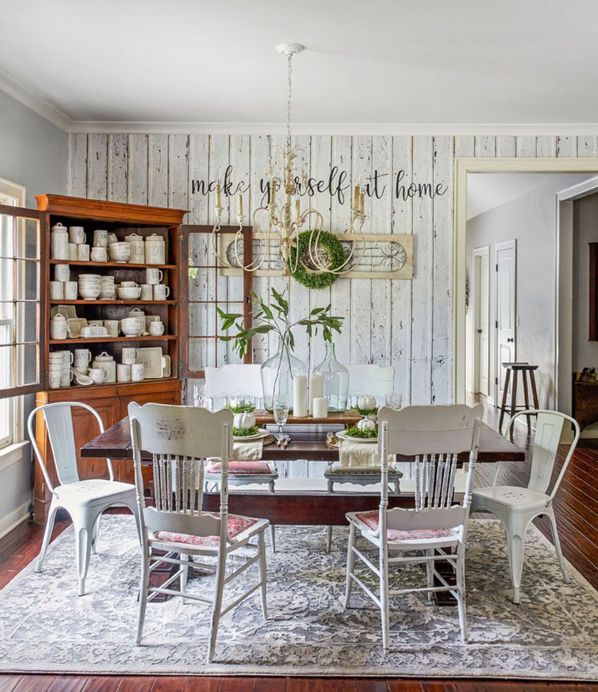 Dining room with white shiplap accent wall. Wooden cabinet displays many cream-colored dishes.