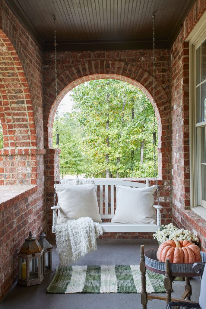 Brick front porch with a white porch swing and green striped mat.