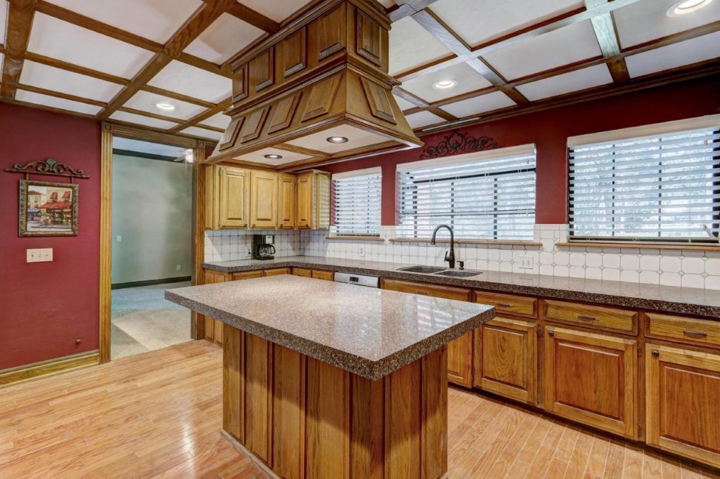 A 1980s large kitchen with dark red paint, tile, oak trim on the ceiling, and oak cabinetry. 