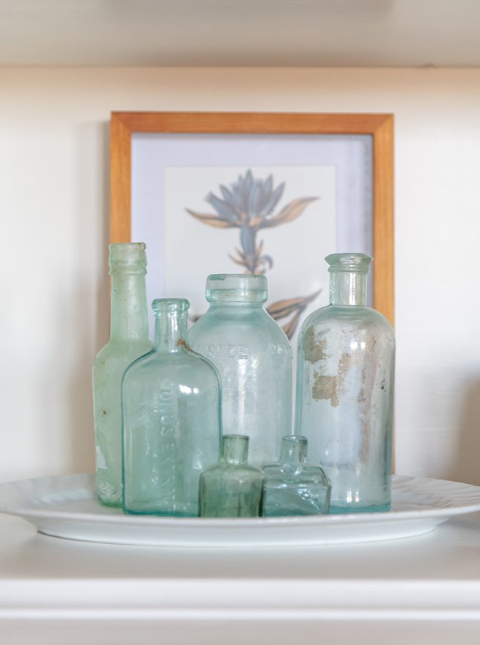 A collection of green glass bottles in front of a picture in a bookshelf.