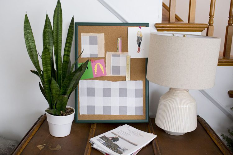 A cork board standing on top if a wooden side table with makeshift paper pockets.
