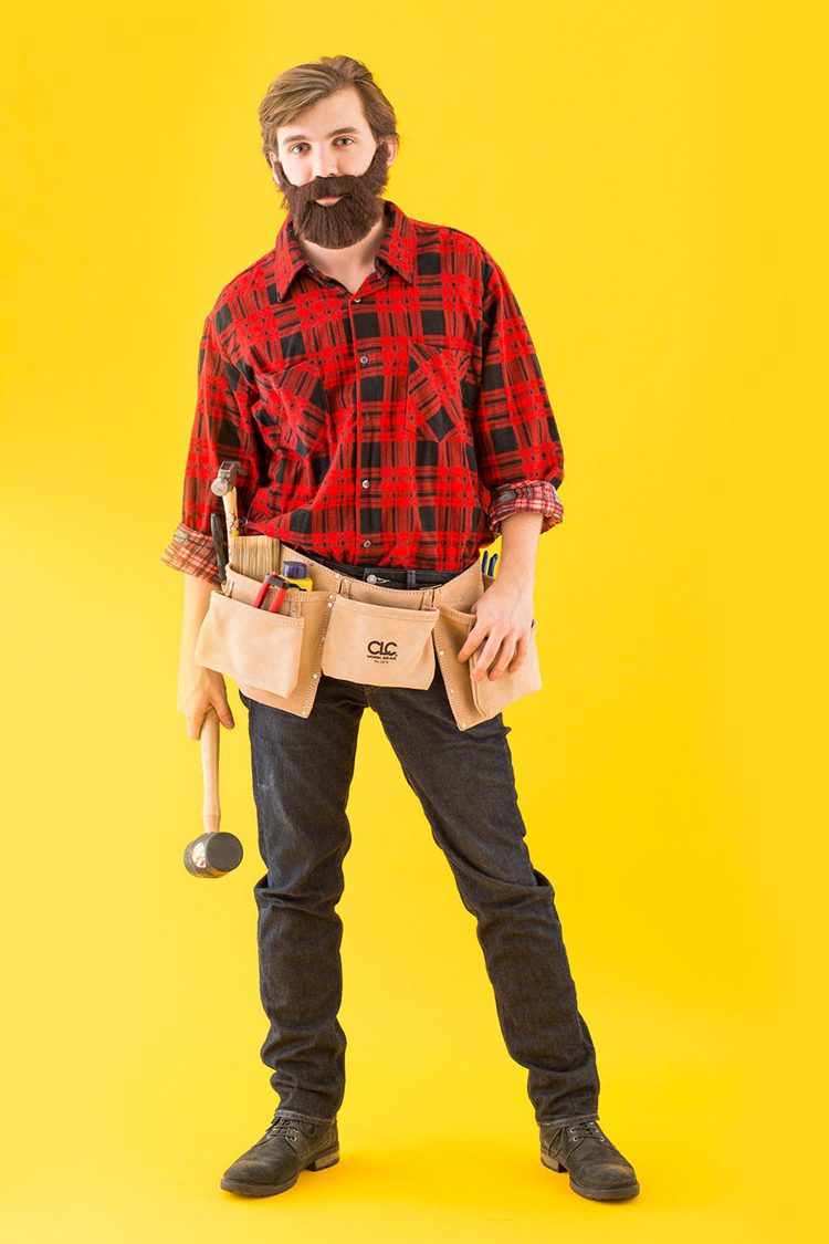 Man dressed in a red and black flannel shirt with a fake beard. He has a leather tool kit tied around his waist and holds a hammer for a DIY Halloween costumes.