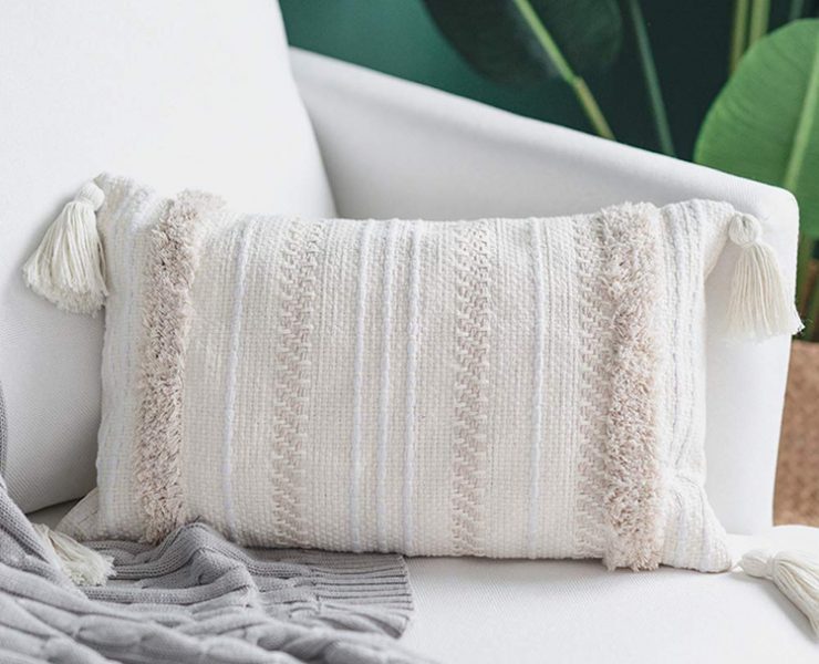 Pillow with different shades of white and off-white stripes and corner tassels.