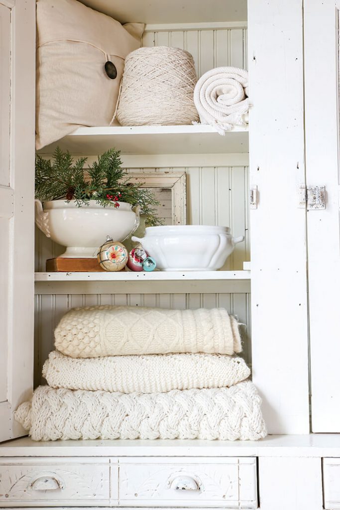 Open cabinet with knit blankets and vintage ornaments