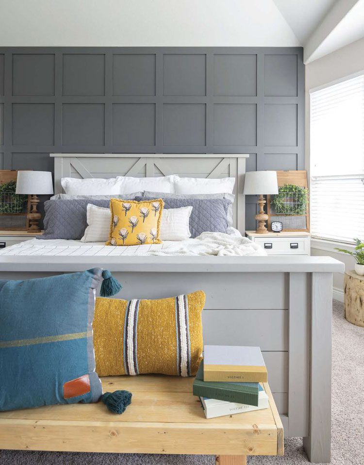 This Texas farmhouse master bedroom is a gray-scale room with yellow, green and dark teal accents in the pillows and faux greenery.