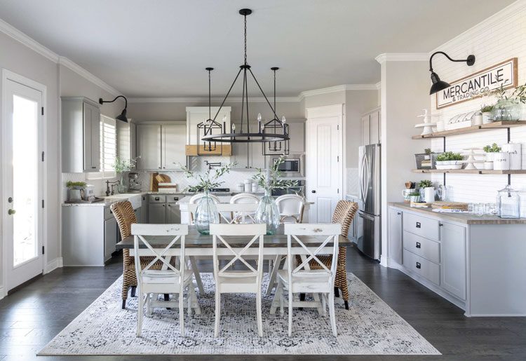This Texas farmhouse kitchen has white chairs, a modern black chandelier and a large neutral accent rug.
