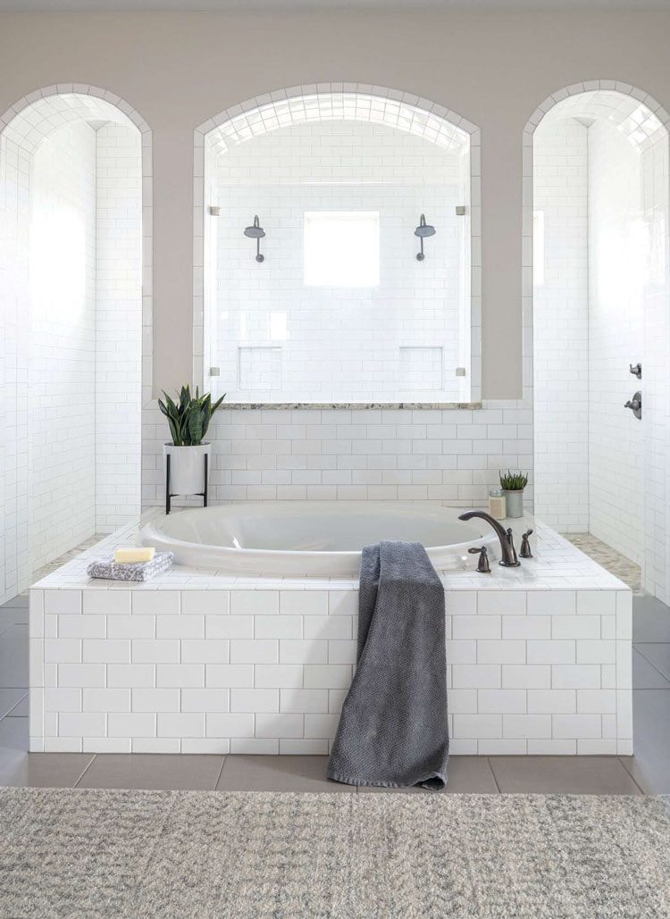 This gray scale bathroom has an open shower plan with two spouts and arched doorway entrances. It also has a bathtub in front of it.