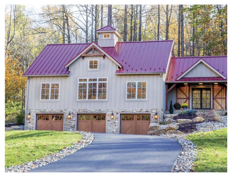 The exterior of this farmhouse example has a purple-tone metal roof with a triple-door garage and a paved driveway leading up to the house.