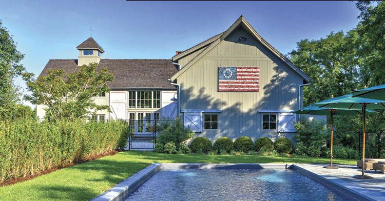 An example of a farmhouse exterior with an American flag artwork applied to the front. Half of the house is olive-green and the other half is white with olive-green trim.