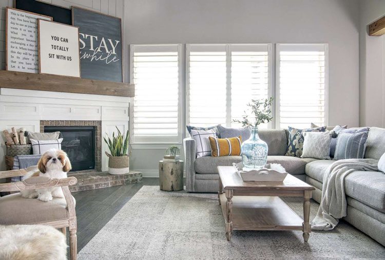 This open floor plan Texas farmhouse boasts comfy gray couches with yellow accent pillows and a rustic wood coffee table.