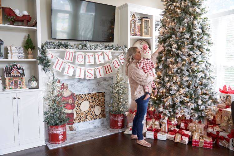 Jenna holding her son in front of their Christmas tree and faux fireplace.