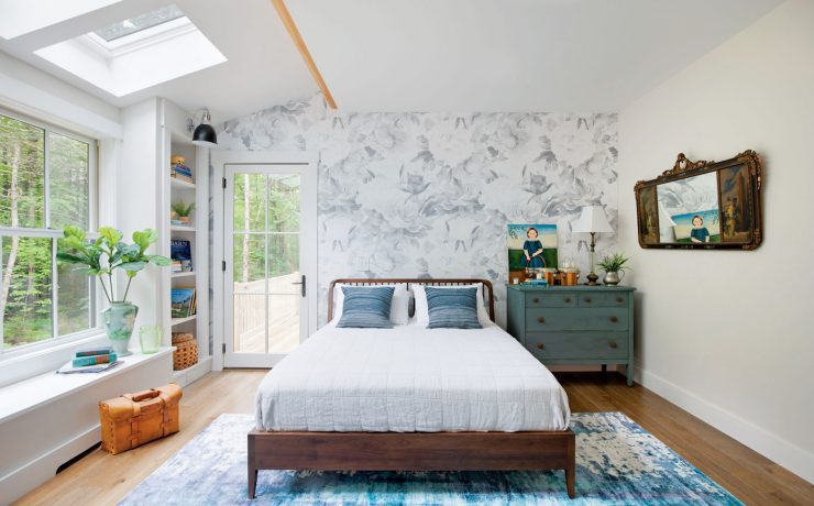 This farm-cottage bedroom shows off the comforts of home with a white comforter, peel-away gray patterned wallpaper and plenty of windows for natural light.