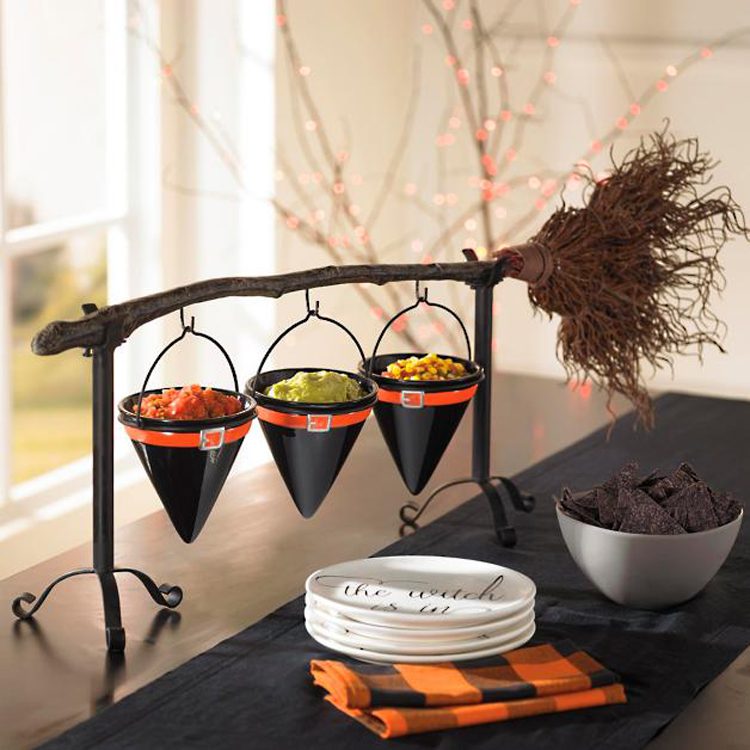 This witch's broom is held up by two black metal legs to allow three ceramic witch hats to hang from the broom handle—ready to be filled with candy!