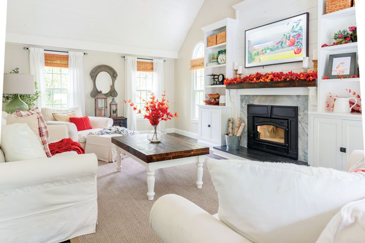 Nina's primarily white, farmhouse style living room has pops of orange fall decor in the pillow, foliage and mantel garland. Beautiful upcycled fall decor!